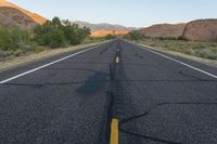 a deserted, empty highway near a barren mountain range in the background are rocks and desert