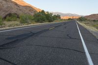 a deserted, empty highway near a barren mountain range in the background are rocks and desert