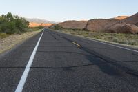 a deserted, empty highway near a barren mountain range in the background are rocks and desert