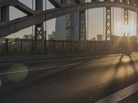 sun behind the arched arch of an old bridge over a road with traffic visible underneath