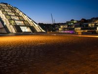 a triangular pyramid sitting on top of a brick road next to some buildings at night