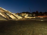 a triangular pyramid sitting on top of a brick road next to some buildings at night