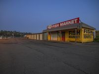 an empty market on the roadside with yellow paint, surrounded by signs for fish and chips