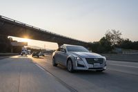 the grey cadillac sedan is driving down the highway with a truck in front of it