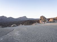 a person walks up the hill in front of a mountain range of large rocks and a mountain