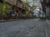 some old buildings near the sidewalk and one is leaning on a fence to pick up something from