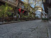 some old buildings near the sidewalk and one is leaning on a fence to pick up something from