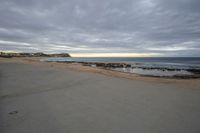 a beach view, from a sidewalk in front of a sunset sky and the ocean