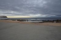 a beach view, from a sidewalk in front of a sunset sky and the ocean