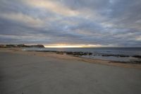 a beach view, from a sidewalk in front of a sunset sky and the ocean