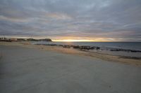 a beach view, from a sidewalk in front of a sunset sky and the ocean