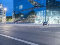 a very large modern looking building by the road with a motorcycle parked in front of it