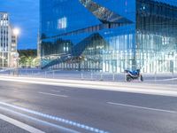 a very large modern looking building by the road with a motorcycle parked in front of it