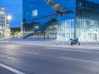 a very large modern looking building by the road with a motorcycle parked in front of it