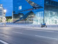 a very large modern looking building by the road with a motorcycle parked in front of it