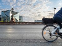 a woman riding a bike across a bridge with tall buildings behind her and the person in the bike is driving