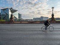 a woman riding a bike across a bridge with tall buildings behind her and the person in the bike is driving