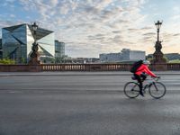 a woman riding a bike across a bridge with tall buildings behind her and the person in the bike is driving