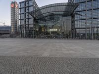 an empty area surrounded by stone bricks, on which two buildings have glass front entrances