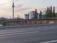 a street view looking at a bridge with a clock tower in the background at sunset