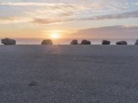 some rocks laying in the dirt on a beach with a sunset and sea in the background