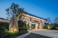 the entrance to a modern home with a big sign and bushes in front of it