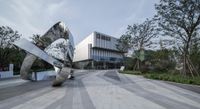 large metal sculptures in front of a museum building with modern architecture, surrounded by trees