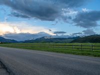 the road is empty during the day and has mountains in the distance as well as a fence