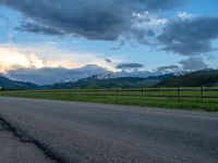 the road is empty during the day and has mountains in the distance as well as a fence