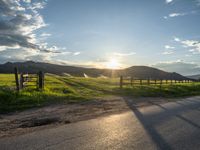 a lone country road is in the countryside area with mountains on both sides and barbed fence between the two sides