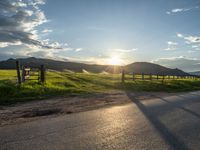 a lone country road is in the countryside area with mountains on both sides and barbed fence between the two sides