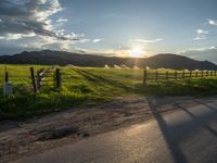 a lone country road is in the countryside area with mountains on both sides and barbed fence between the two sides