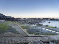 the view is full of people on the water, and the beach has small boats and a grassy area with large rocks