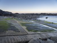 the view is full of people on the water, and the beach has small boats and a grassy area with large rocks