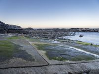 the view is full of people on the water, and the beach has small boats and a grassy area with large rocks