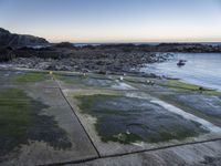 the view is full of people on the water, and the beach has small boats and a grassy area with large rocks