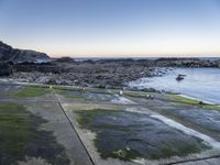 the view is full of people on the water, and the beach has small boats and a grassy area with large rocks