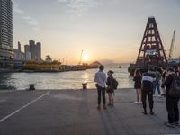 a group of people that are standing in the street near water watching the sun set