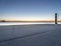 a concrete structure sits along the water on an empty beach during sunrise with city skyline in background