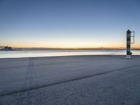 a concrete structure sits along the water on an empty beach during sunrise with city skyline in background