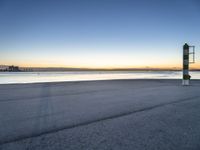 a concrete structure sits along the water on an empty beach during sunrise with city skyline in background