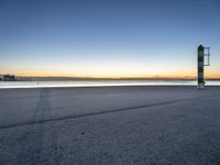 a concrete structure sits along the water on an empty beach during sunrise with city skyline in background