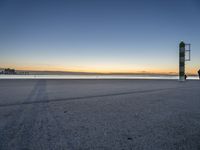 a concrete structure sits along the water on an empty beach during sunrise with city skyline in background