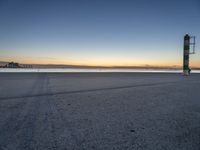 a concrete structure sits along the water on an empty beach during sunrise with city skyline in background