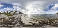 a fish eye view of the water and shore line and some rocks and trees in a grassy area