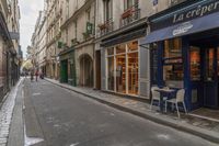 a narrow street in paris with restaurants on the side of it, a person stands at the doorway