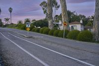 an empty street with a sign indicating to stop traffic in front of some houses at sunset