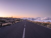 an empty winding road on a mountain with the sun set above the mountains in the background