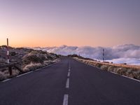 an empty winding road on a mountain with the sun set above the mountains in the background