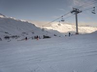 skiers ride up a snowy slope in the mountains with a sky lift overhead above